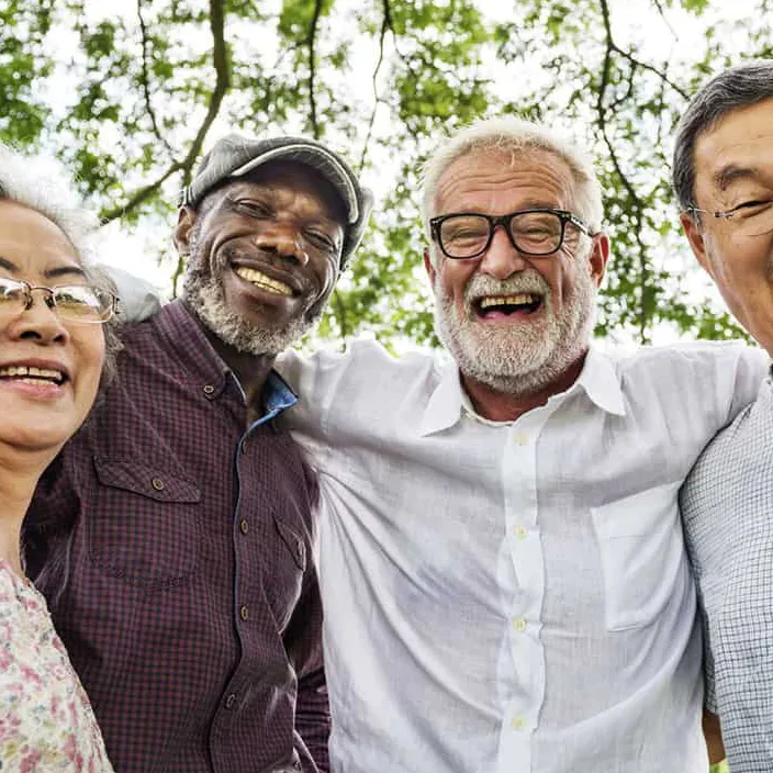 Group of retirees smiling with their arms wrapped around each others' shoulders.