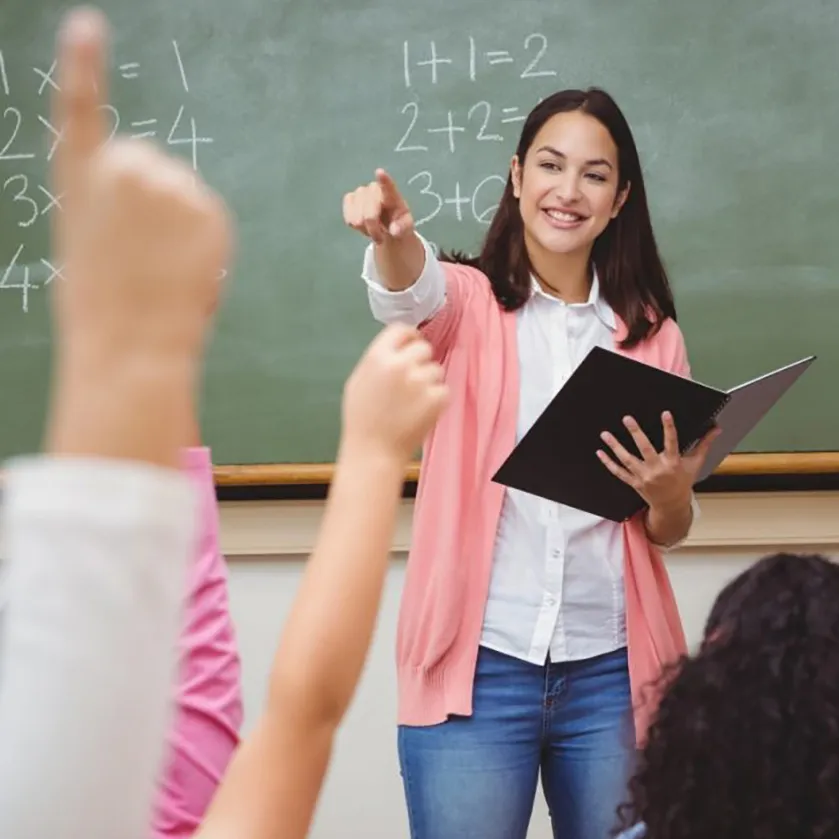 Female teacher in a classroom setting standing in front of a chalkboard.